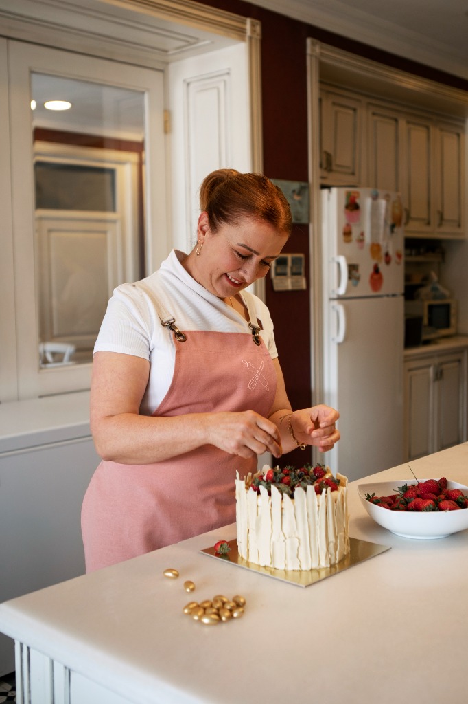 Confeiteira artesanal decorando um bolo com morangos frescos na cozinha