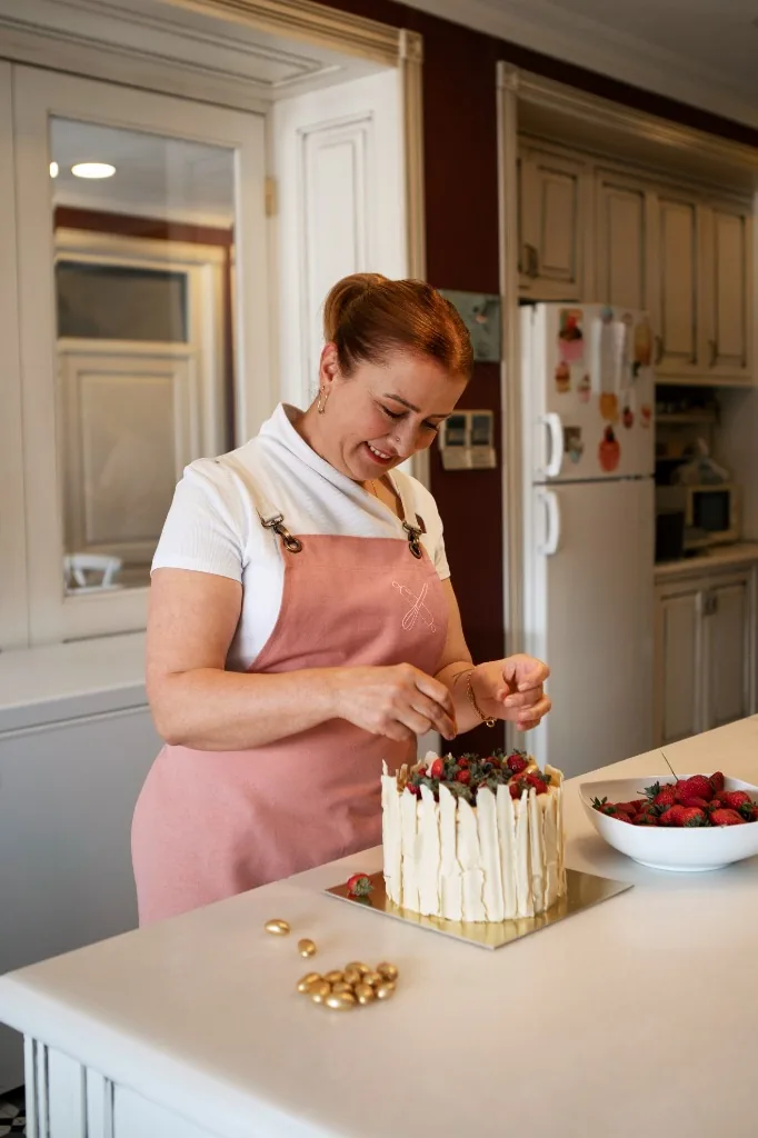 Confeiteira artesanal decorando um bolo com morangos frescos na cozinha